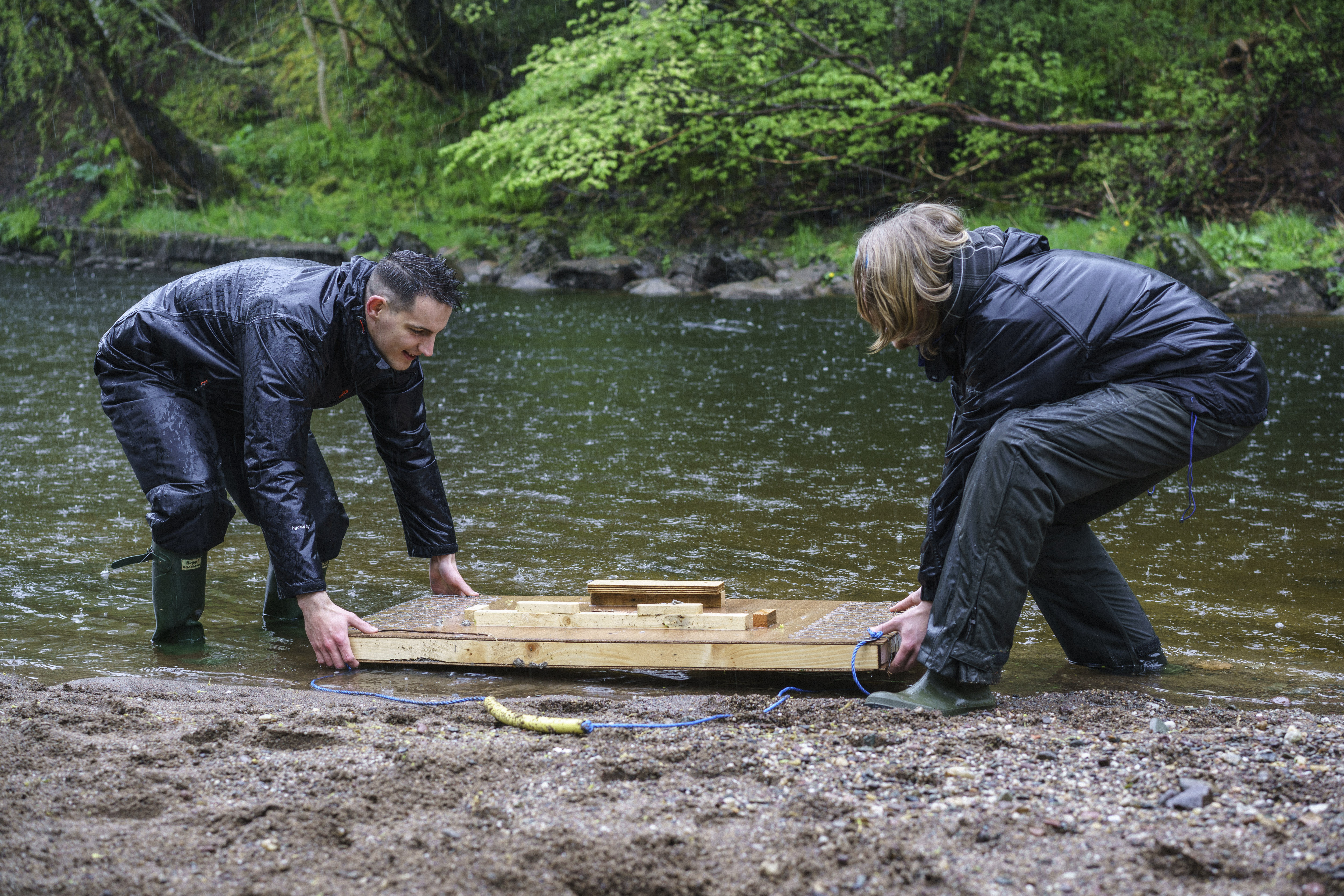 Volunteer and Project Officer lifting a mink raft into a river